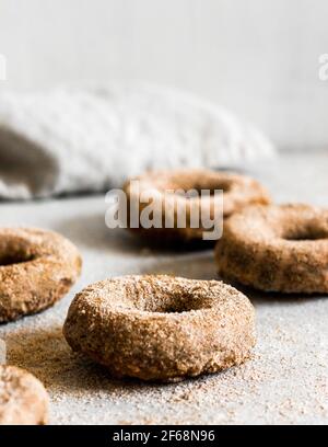 Im Ofen gebackene, flauschige, hausgemachte vegane Apfelmost-Donuts, die mit Zimt-Zucker-Vereisung bedeckt sind. Stockfoto