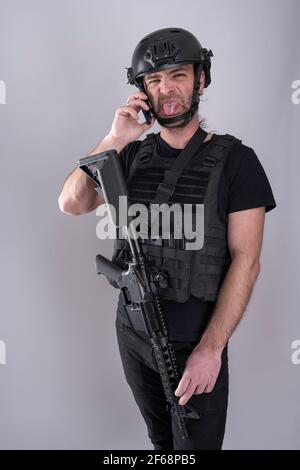 Stehender Mann für Airsoft mit Helm und Schutzweste ausgestattet Hält seine Zunge an die Kamera und macht einen Grimace beim Bestätigen des Negoc Stockfoto
