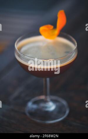 Dunkler Cocktail mit orangefarbenem Touch in dunkler Bar-Atmosphäre. Stockfoto