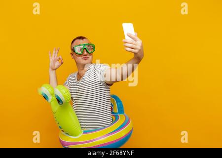 Mann trägt Unterwasser-Maske, gestreiftes Hemd, schwimmen Runden Blick in das Telefon, wobei sehr emotional Selfie, während lächelnd auf gelbem Hintergrund Stockfoto