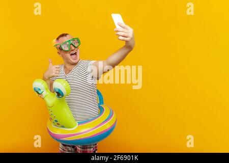 Mann trägt Unterwasser-Maske, gestreiftes Hemd, schwimmen Runden Blick in das Telefon, wobei sehr emotional Selfie, während lächelnd auf gelbem Hintergrund Stockfoto