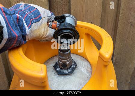 Eine Hand mit Handschuh montiert einen Niederdruck-Gasregler mit Schlauch an einer Gasflasche, Dänemark, März 30, 2021 Stockfoto