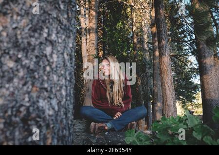Blonde Frau sitzt friedlich in der Mitte eines Waldes Stockfoto