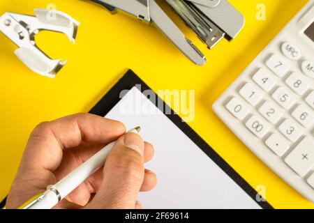 Mock up Bürozubehör auf gelbem Hintergrund flach Lay of Business Gadgets und Hand von unbekannten Mann hält Stift schreiben Stockfoto