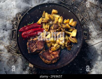 Bratpfanne mit Kartoffeln, Steaks und Paprika auf dem Feuer Stockfoto