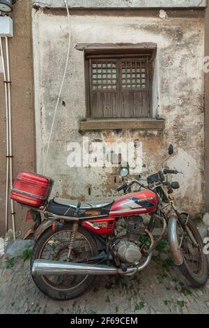 Tongli, China - 2. Mai 2010: Nahaufnahme des geparkten roten Honda 125cc Motorrads gegen schmutzige weiße Wand mit braunem Holz bedecktem kleinen Fenster. Stockfoto