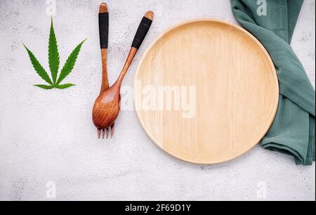 Essen konzeptuelles Bild eines Cannabisblattes mit Löffel und Gabel auf weißem Beton Hintergrund. Stockfoto