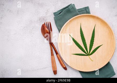 Essen konzeptuelles Bild eines Cannabisblattes mit Löffel und Gabel auf weißem Beton Hintergrund. Stockfoto