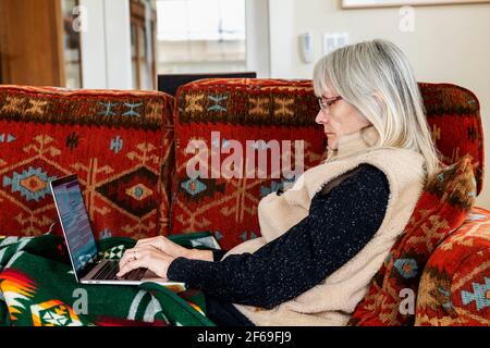 Ältere Frau sitzt auf der Wohnzimmercouch und arbeitet auf dem Laptop Computer Stockfoto