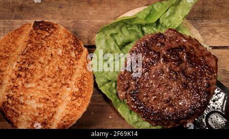 Salat und frisch gegrilltes Fleisch auf ein Burger-Brötchen geben - Vorbereitung eines Hamburgers Stockfoto