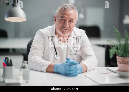 Ein Professor für medizinische Wissenschaften führt ein Praktikum in einem Krankenhaus durch, er sitzt an einem Tisch und schaut auf die Kamera. Stockfoto