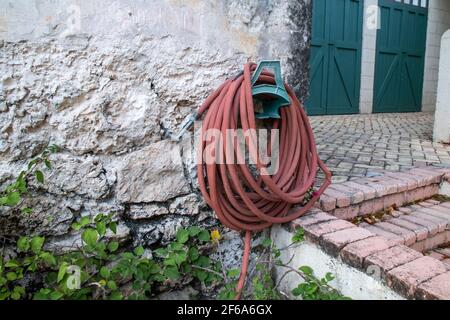 Ein aufgewickelter sienna verbrannte orangefarbenen Gartenschlauch gegen eine alte Backsteinmauer in Bridgetown, Barbados, Gartenpflanzer unten. Stockfoto