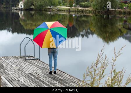 Mädchen steht auf Jetty mit bunten Regenschirm Stockfoto