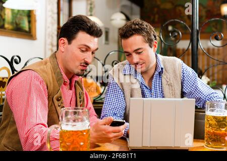 Zwei Freunde in bayerischen Kneipe in traditioneller Kleidung auf einem Tisch in einer Kneipe mit laptop Stockfoto