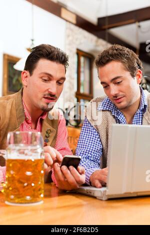 Zwei Freunde in bayerischen Kneipe in traditioneller Kleidung auf einem Tisch in einer Kneipe mit laptop Stockfoto