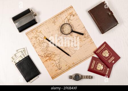 Weltkarte, Bleistift, Lupe, zwei Pässe, Tagebuch, Schwarze Brieftasche mit Geld und eine Flasche auf einem weißen Holztisch. Inschrift - Reisepass Russisch Stockfoto