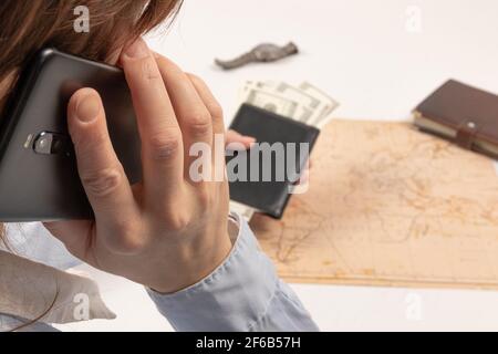 Ein Teil eines Mädchens, das am Telefon spricht, hält sich fest Sie hat eine schwarze Brieftasche mit Geld auf dem Hintergrund Von einem weißen Holztisch mit einem Tagebuch und einem Armbanduhr Stockfoto