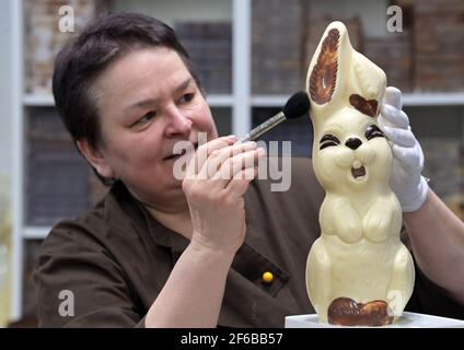 30. März 2021, Brandenburg, Himmelpfort: Sylke Wienold, Leiterin der Himmelpforter Chocolaterie, entfernt mit einem weichen Pinsel störende Partikel aus einem Hasen aus leichter Schokolade. Im kleinen Familienbetrieb im Landkreis Oberhavel gibt es rund 700 Süßwaren; zu Ostern kommen Eier, Kaninchen, Schafe und andere Figuren aus der hellen oder dunklen Schokolade dazu. Der ehemalige Informatiker hat die Zeit der Corona-Sperre genutzt, um einen "Click-and-Collect-Shop" einzurichten. Nach Ostern wird der Laden allerdings vorerst schließen müssen, denn ohne Tourismus und Gastronomie gibt es t Stockfoto