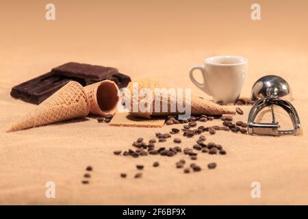 Appetitliches Mandeleis, umgeben von unscharfen Kaffeebohnen, Kaffeetassen und Schokoladenstückchen: Selektiver Fokus. Eiscreme-Konzept. Stockfoto