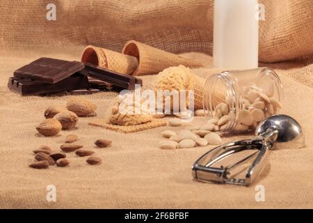 Nougat-Eisschaufeln umgeben von verschiedenen Mandeln und Schokoladenstückchen: Selektiver Fokus und Nahaufnahme. Eis- und Süßwarenkonzept. Stockfoto