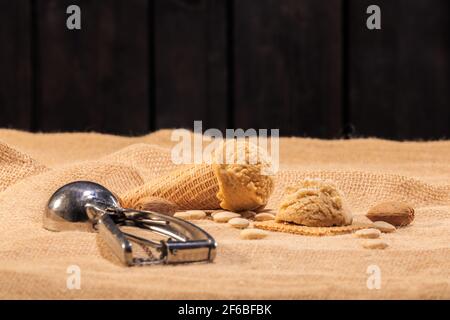 Appetitliches Eis, umgeben von Mandeln, und eine Eisportionierung auf einem unscharfen Hintergrund: Selektiver Fokus. Eiscreme-Konzept. Stockfoto