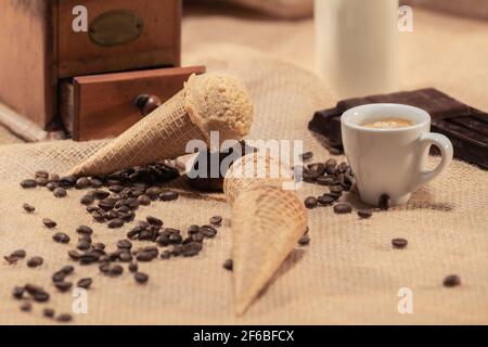 Verführerisches Mandeleis, umgeben von Kaffeebohnen, einer Tasse Kaffee und Schokoladenstückchen: Selektiver Fokus und Nahaufnahme. Eiscreme-Konzept. Stockfoto