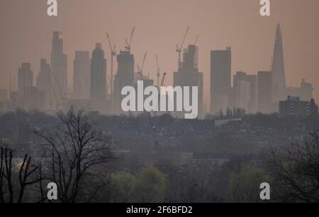 Wimbledon, London, Großbritannien. 31. März 2021. Leichter Nebel im Morgengrauen bei einem Blick über flache Vorstadthäuser auf ferne Wolkenkratzer und Baukräne in der City of London, bevor es in der Hauptstadt wieder zu Sonnenschein kommt. Quelle: Malcolm Park/Alamy Live News Stockfoto