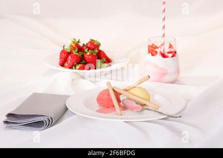 Verlockende Eisschaufeln mit Waffelröhrchen auf einem Teller, mit einem unkonzentrierten Glas Schlagsahne und Erdbeeren. Selektiver Fokus. Dessert-Konzept. Stockfoto
