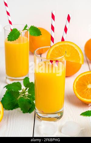 Zwei Gläser Orangensaft mit Röhrchen, Minze und frischen Orangen auf weißem Hintergrund. Stockfoto