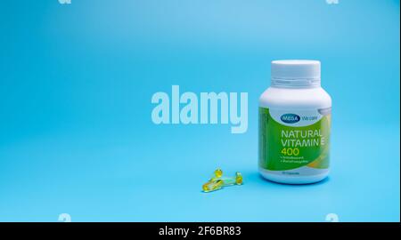 CHONBURI, THAILAND-JANUARY 31, 2021 : Mega We care Natural Vitamin E 400 IU in PP-Plastikflasche und vier weiche Gelatine Kapsel auf blauem Hintergrund. Stockfoto