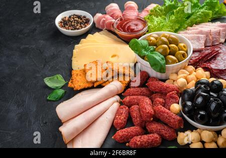 Eine große Auswahl an Wurst und Käse wird auf einem Schiefertafel auf schwarzem Hintergrund geschnitten. Stockfoto