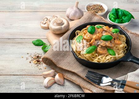 Pasta mit Pilzen, Huhn und Basilikum auf einem hellen Holztisch mit Platz zum Kopieren. Stockfoto