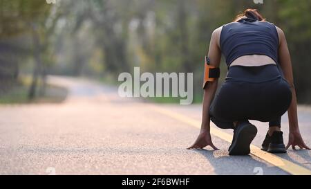 Rückansicht einer sportlichen Frau, die sich auf einen Lauf bei Sonnenuntergang im Park vorbereitet. Stockfoto