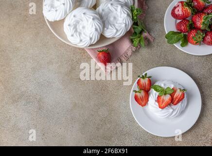 Mini-Baiser-Nest mit frischen Erdbeeren und Minze auf einem Teller, leeres Baiser-Nest und Erdbeeren auf Betongrund. Selektiver Fokus. Draufsicht Stockfoto