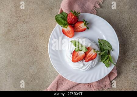 Mini Pavlova Meringue Kuchen mit Erdbeeren und Minze auf einem Teller, Beton Hintergrund. Draufsicht. Selektiver Fokus. Stockfoto