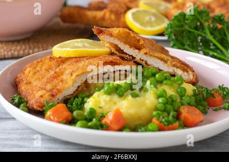 Ein Teller mit gebratenem wiener Schnitzel, serviert mit frischen Kartoffelpüree und gebutterten Erbsen und Karotten auf einem Teller. Nahaufnahme Stockfoto