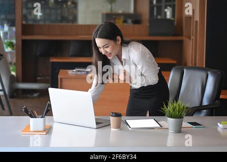 Eine glückliche Geschäftsfrau, die auf den Bildschirm eines Laptops schaut und sich begeistert fühlt, feiert ein erfolgreiches Projekt. Stockfoto