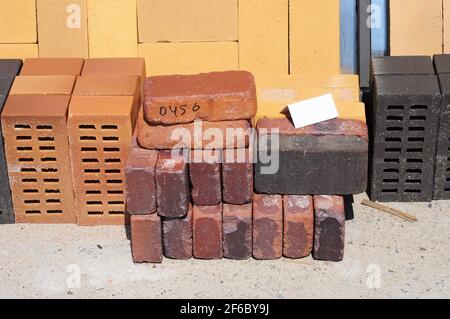 Farbige Bausteine, Ziegelsteine und Betonfertiger (Pflastersteine) oder Terrassenblöcke, die auf Paletten zum Verkauf auf Metallregalen im Freien gelagert werden. Stockfoto