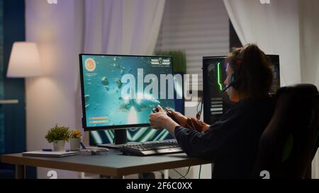 Rückansicht Aufnahme von aufgeregt Frau Gamer Streaming Online-Videospiele und Wining spielen auf RGB leistungsstarken Computer mit Wireless-Controller. Spieler mit Kopfhörern, der den Sieg im Spielezimmer feiert Stockfoto