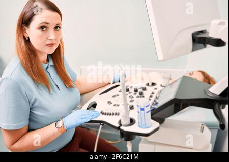 Nette Ärztin, die Ultraschallverfahren in der Klinik durchführt. Stockfoto