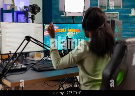 Afrikanischer Spielstreamer feiert den Sieg mit Multispielern nach dem Sieg. Online-Streaming Cyber-Performance während Videospiele Turnier in zu Hause mit Neonlicht. Stockfoto