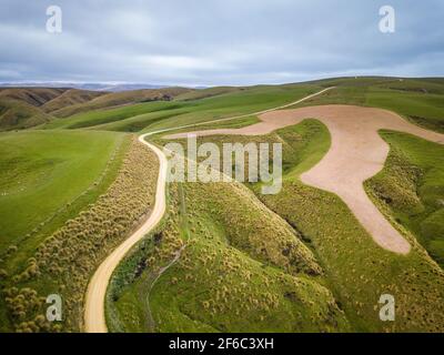 Leere Schotterstraße, die sich in grüner Landschaft schlängelt. Luftaufnahme von Neuseeland fantastische Landschaften und Landschaften. Stockfoto