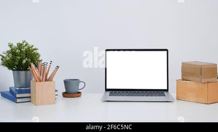 Vorderansicht eines Computer-Laptops mit leerem Bildschirm, Hauspflanze, Bleistifthalter und Schachteln auf weißem Tisch. Stockfoto