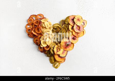 Herz aus getrockneten geschnittenen Pflaumen, Kiwi, Pfirsich-Chips auf weißem Hintergrund. Herbsternte. Heimtrocknung. Snack vegan frei von Zucker Lebensmittel. Stockfoto