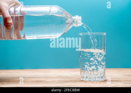 Sauberes, gesundes, kühles Wasser strömt aus einer Plastikflasche auf blauem Hintergrund in ein Glas. Stockfoto