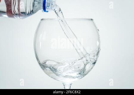 Reines gesundes Mineralwasser wird aus einer Flasche in ein transparentes Glas auf weißem Grund gegossen. Nahaufnahme. Stockfoto