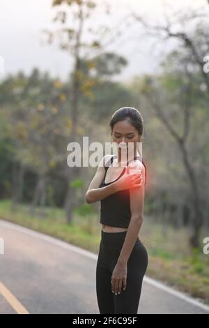 Die Sportlerin hat beim Joggen im Park Schmerzen und legt ihre Hand auf die Schulter. Stockfoto