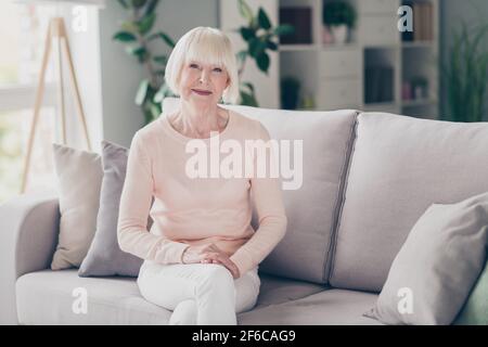 Foto-Portrait ältere Frau mit weißen Haaren sitzt auf dem Sofa In gemütlicher Atmosphäre in stilvoller Kleidung Stockfoto