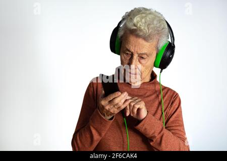 Ältere Frau, die Musik mit Kopfhörern und Smartphone hört. Blick auf Handy-Bildschirm mit Handy-Player-App Online-Musik hören, lernen foreig Stockfoto