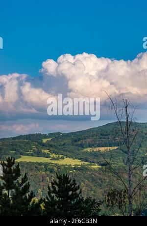 Massive Wolken - Cumulus congestus oder aufragender Cumulus - auf Der blaue Himmel über hügeliger Landschaft Stockfoto